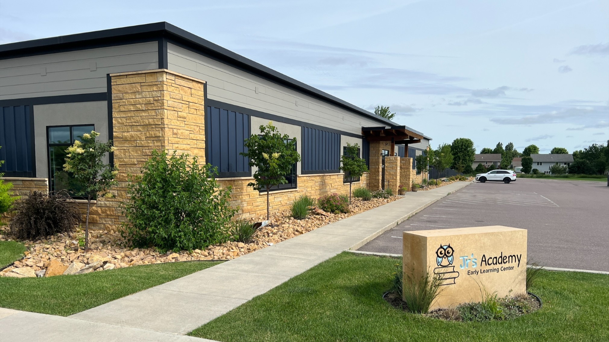 Exterior view of the Jr’s Academy addition with stone and metal siding, landscaped walkway, and main entrance, constructed by Rice Companies.